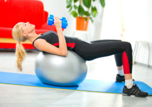 Woman doing fitness exercises with dumbbells and ball at home